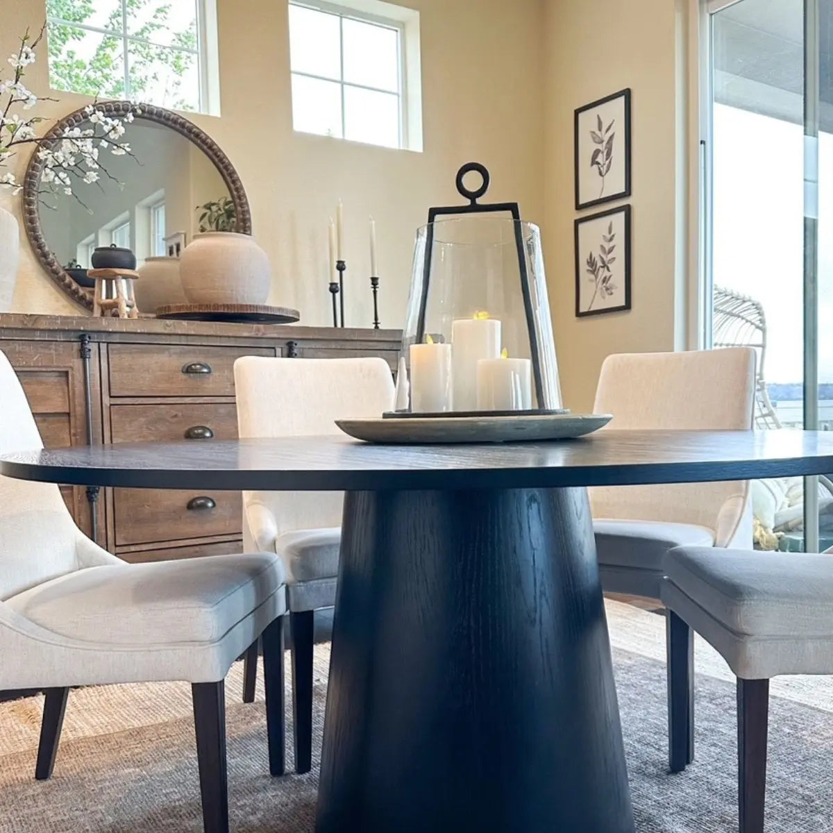 Orchid Oak Pedestal Dining Table with beige chairs, wooden cabinet, round mirror in cozy dining room.