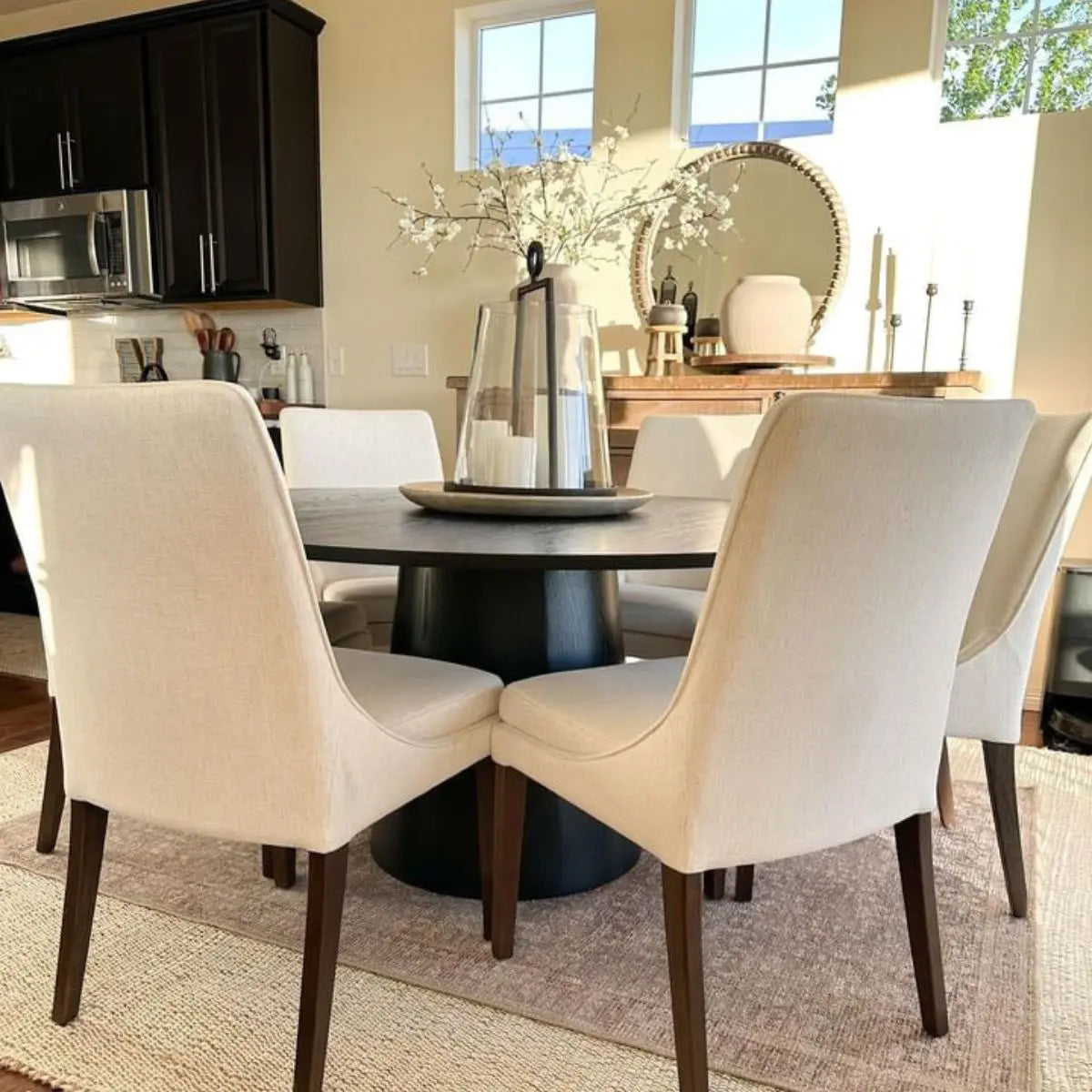 Orchid 60" Oak Round Pedestal Dining Table with beige chairs, light walls, wooden sideboard.