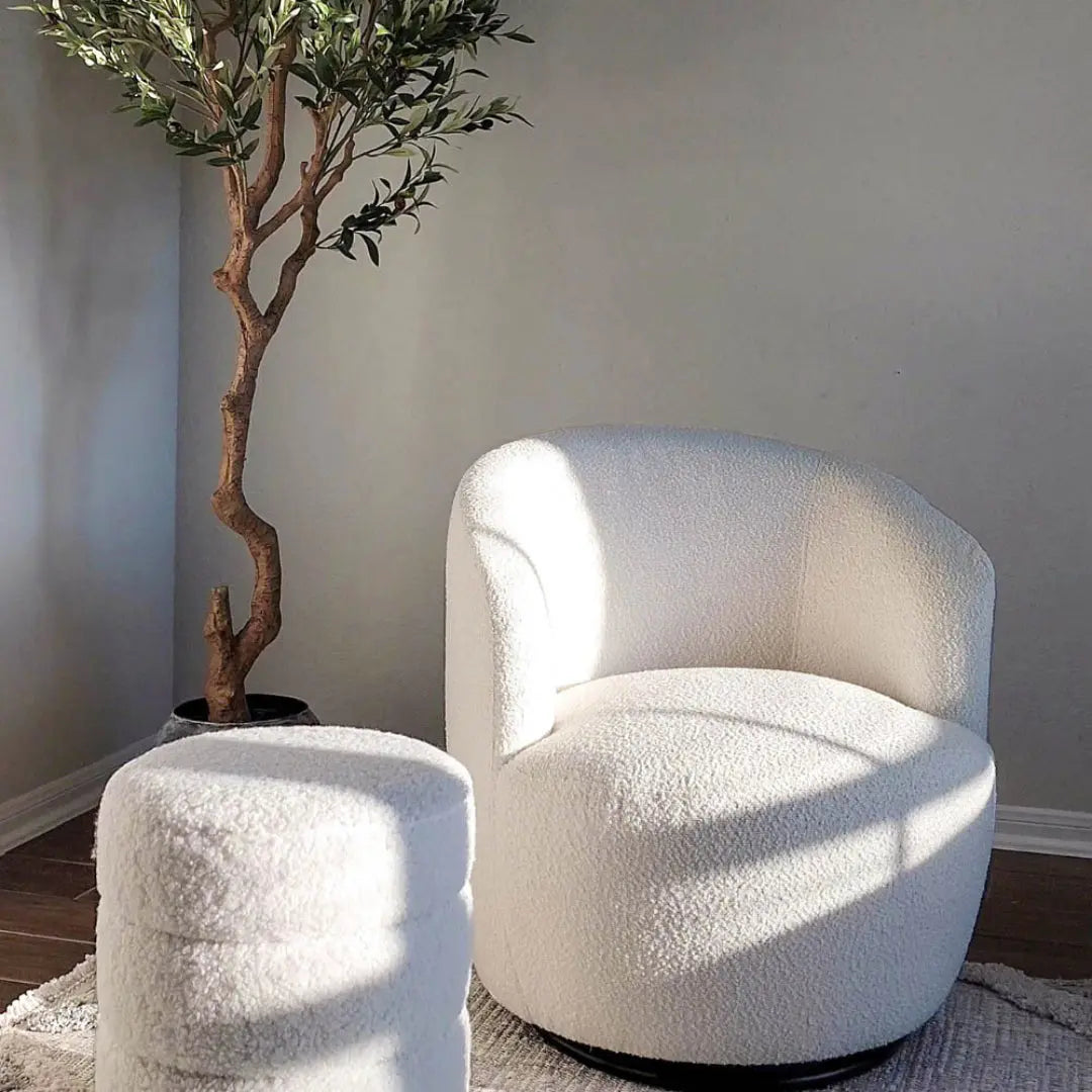 Bella Modern White Boucle Swivel Barrel Chair with ottoman, on hardwood floor beside an olive tree.