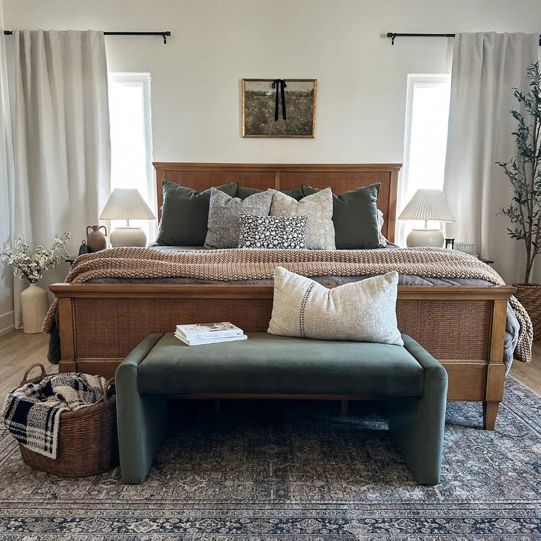 Kaia bench in bedroom with wood bed, white walls, woven basket, green cushion, patterned rug.