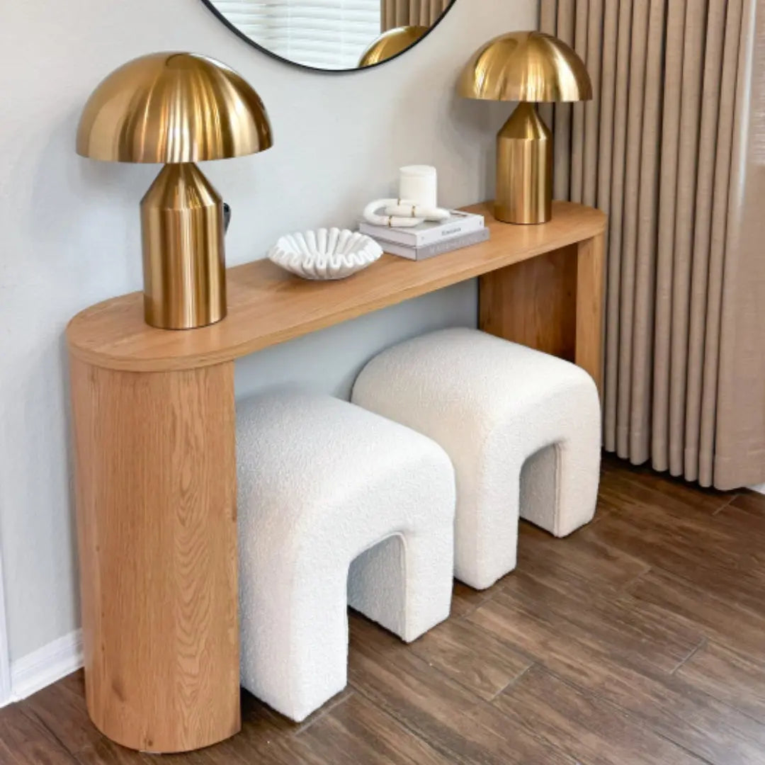 Dwen 60" oval console table with gold lamps, white stools, wood flooring, light gray walls.