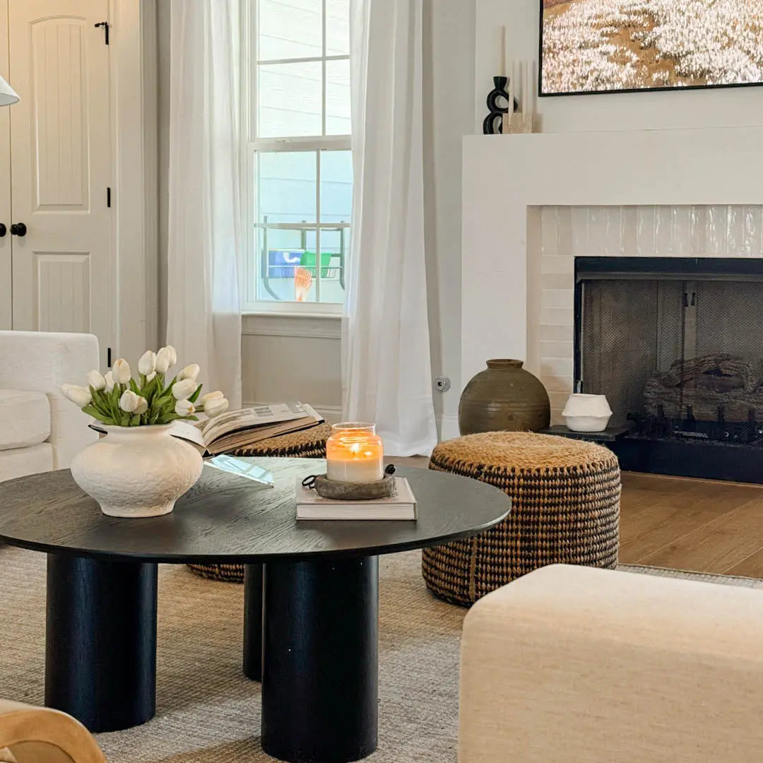 Baguette Modern Black Oak Wood Coffee Table in cozy living room with beige sofa, fireplace, woven stools.