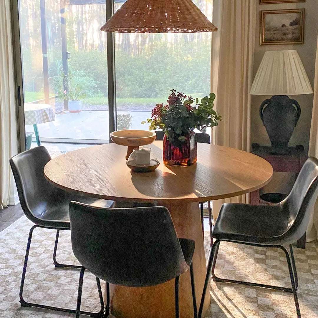 Dwen Modern Round Pedestal Dining Table in cozy dining room, wicker lamp, floor-to-ceiling windows.