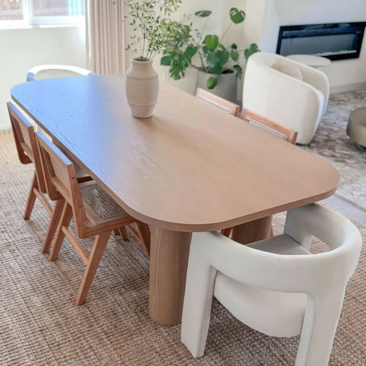 Large oak dining table with beige chairs, in cozy living room with beige sofa and rug.