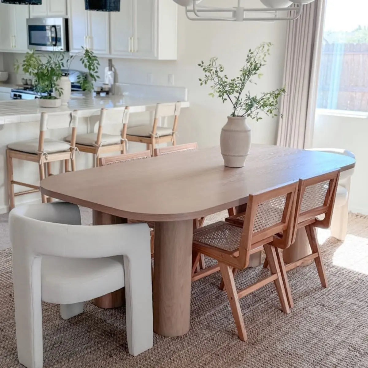 Modern oak dining table with chairs, neutral rug, and light curtains in a bright dining room.