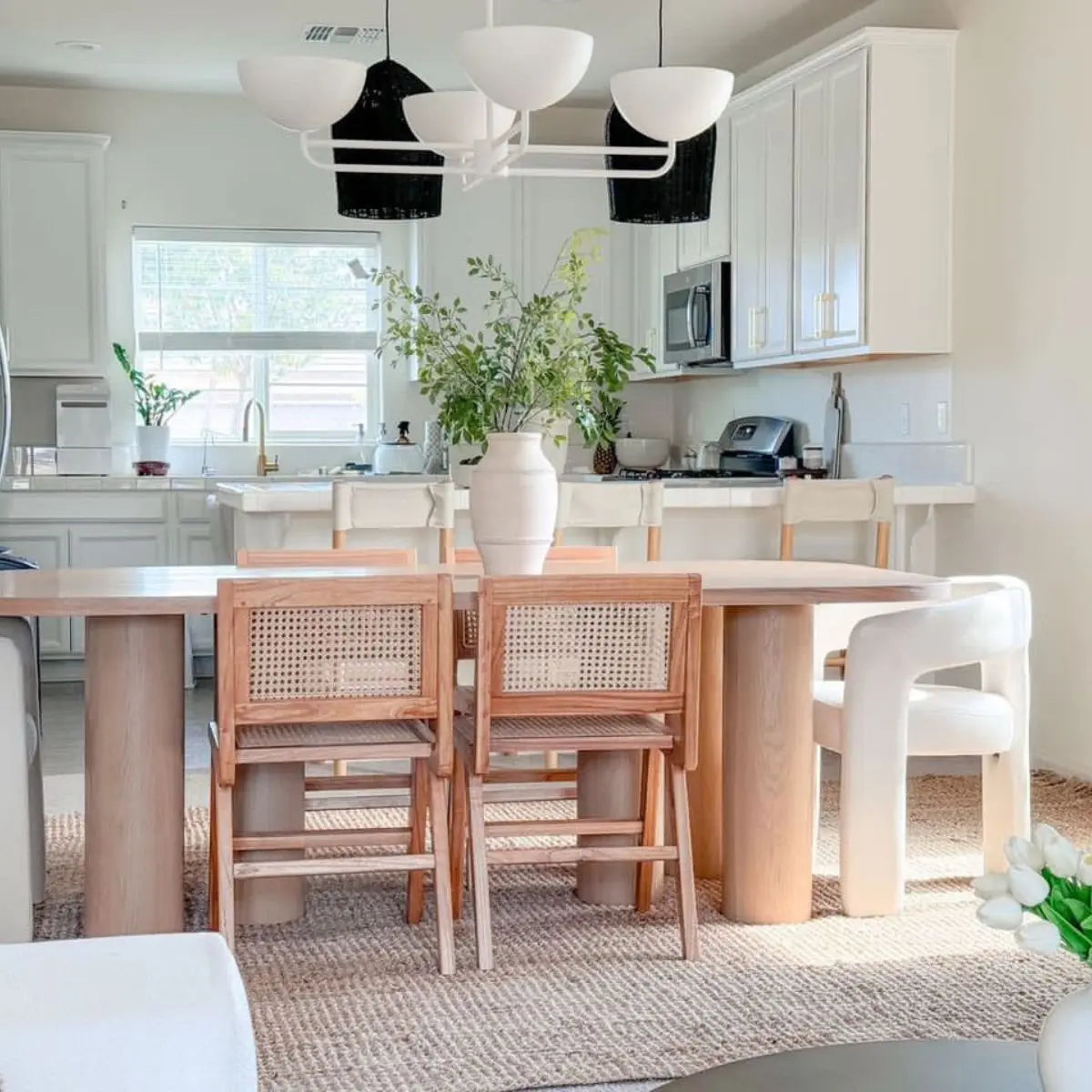 Modern Oak Dining Table with woven chairs, white walls, pendant lights, and beige rug in kitchen.