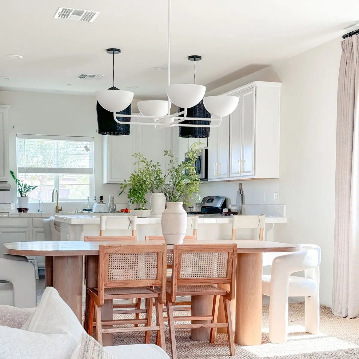 Modern oak dining table in bright kitchen, white cabinets, rattan chairs, minimalist decor.