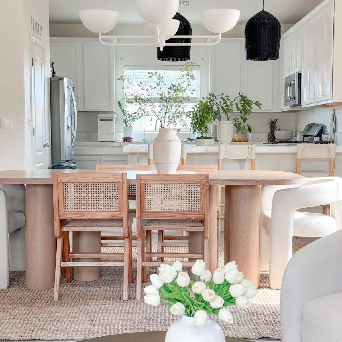 Baguette Modern Oak Dining Table in kitchen with wicker chairs, white cabinets, and pendant lights.