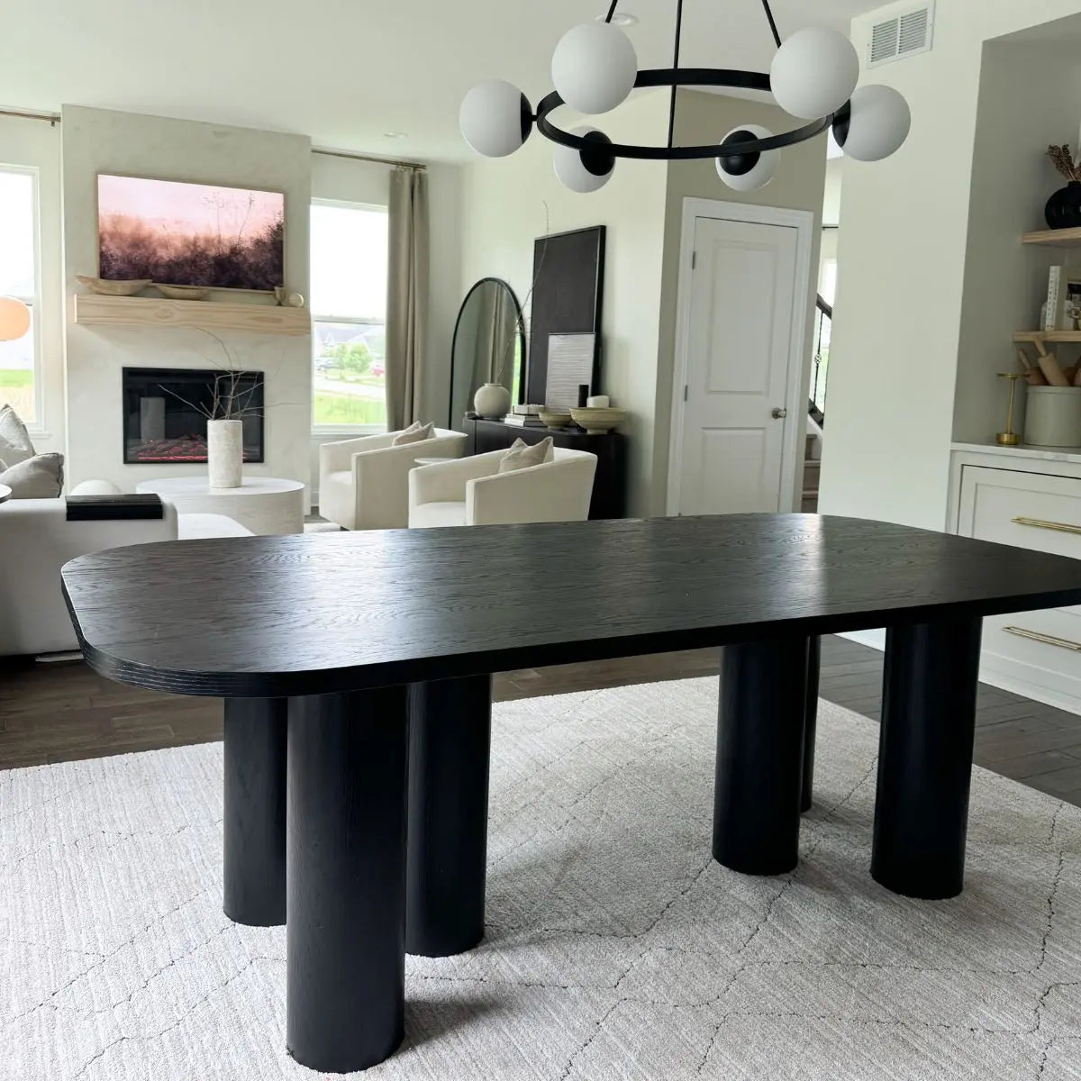 Modern oak dining table with black finish in elegant living room; features chandelier and beige sofa.