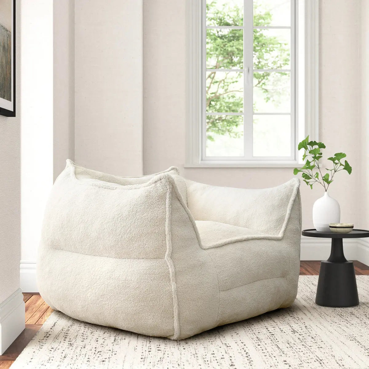 Creamy Boring Upholstered Teddy Fabric Bean Bag Chair, white walls, carpeted room, round black side table.