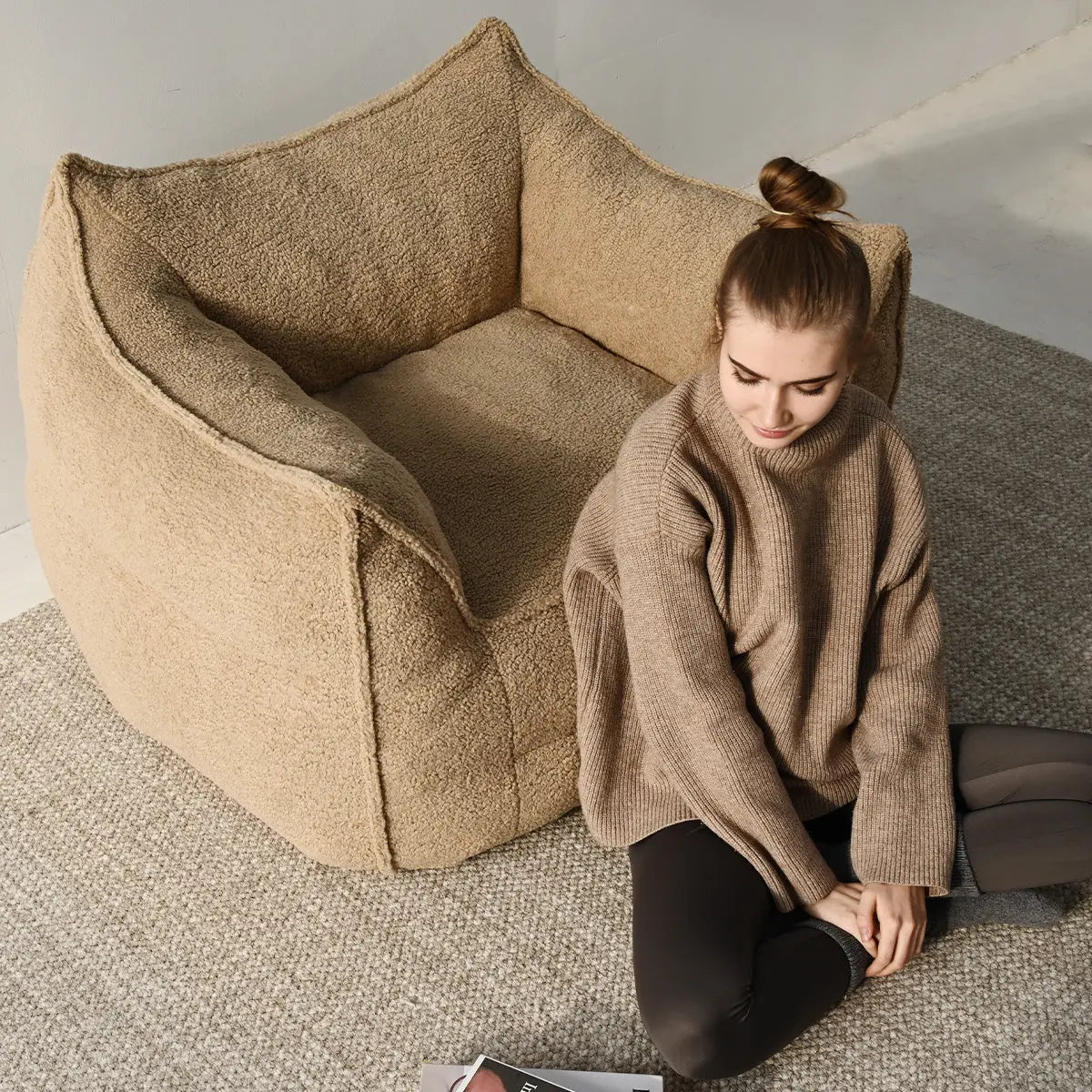 Boring Teddy Fabric Bean Bag Chair with cozy brown sweater in modern living room, grey carpet floor.