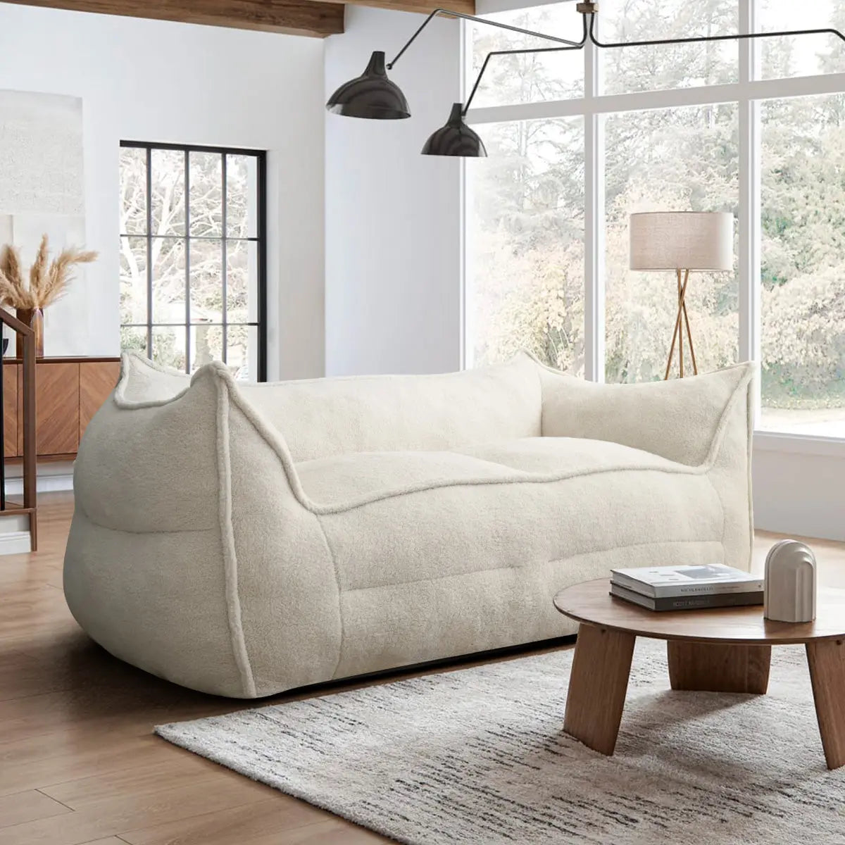 Cream teddy fabric loveseat sofa in modern living room with wood floor, rug, and large windows.