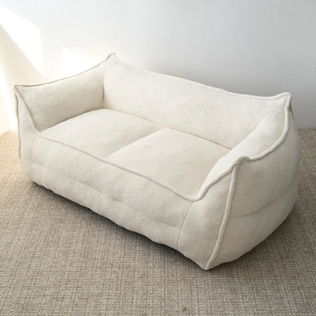 Cream-colored teddy fabric bean bag loveseat sofa on beige carpet flooring in minimalist room setting.