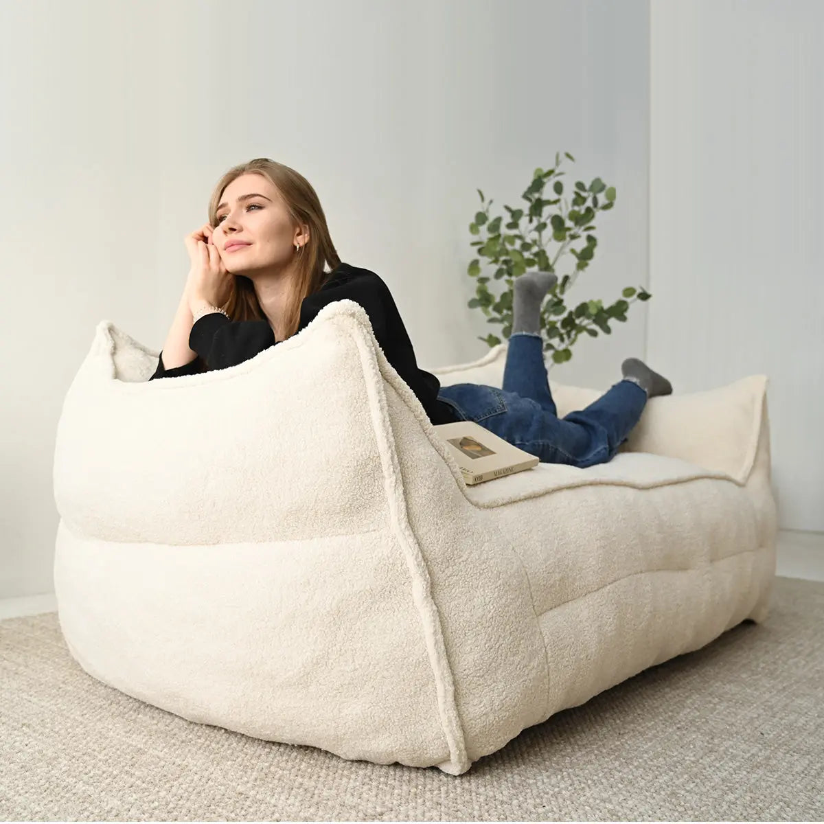 Woman relaxing on Boring Large Teddy Bean Bag Loveseat Sofa in cream, neutral wall, carpet flooring.