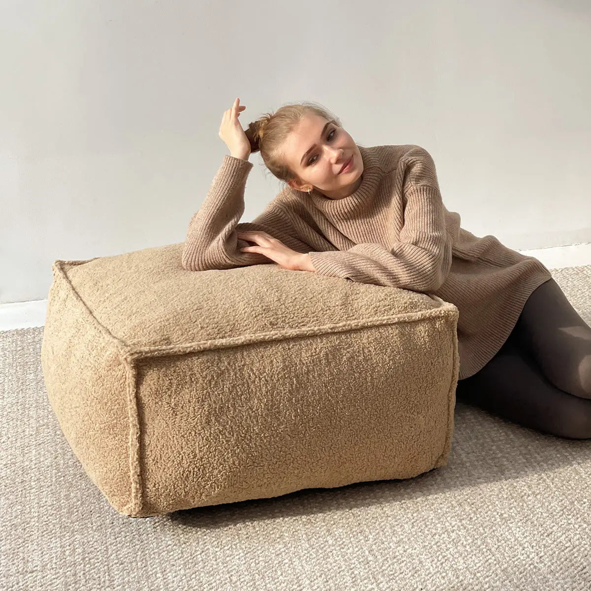 Tan Boring Teddy Square Bean Bag Ottoman with beige carpet, off-white wall, relaxed setting.