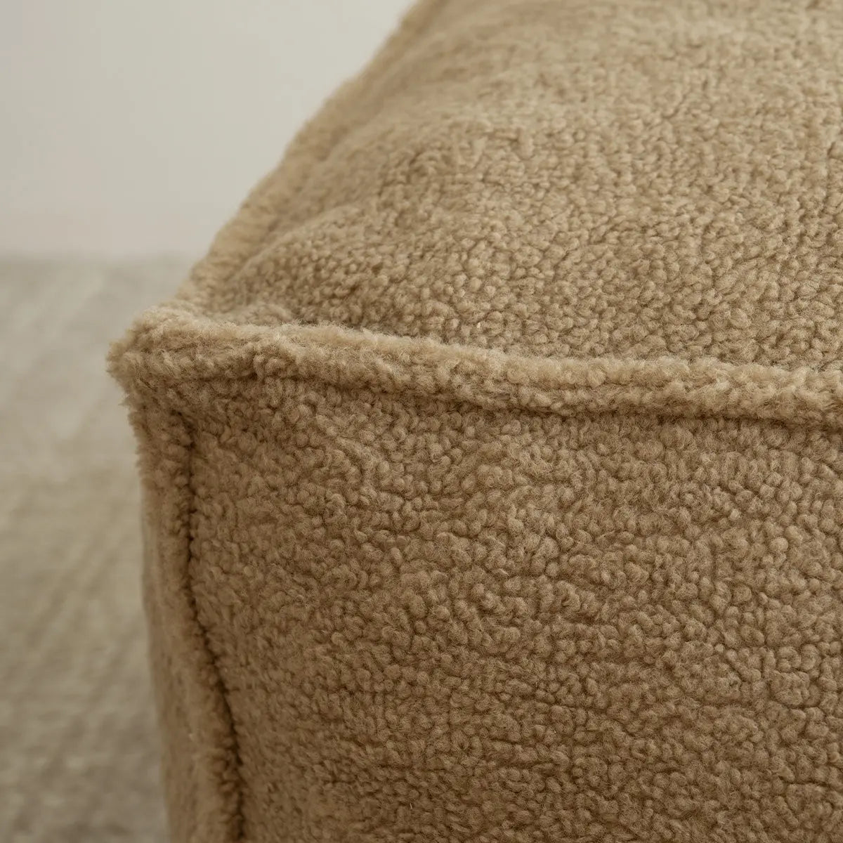 Close-up of beige Boring Teddy Fabric Bean Bag Chair material on textured carpet flooring.