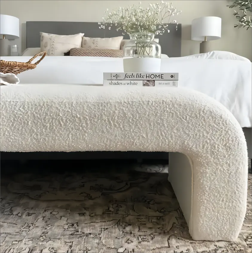 Modern velvet waterfall bench in bedroom with plush neutral bedding, patterned rug, and elegant decor.