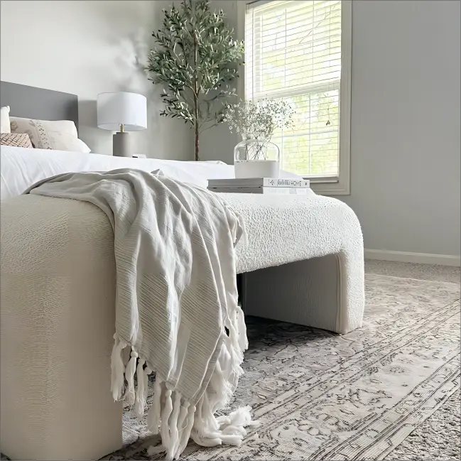 Lily Modern Velvet Accent Waterfall Bench in bedroom with patterned rug, gray headboard, and soft lighting.