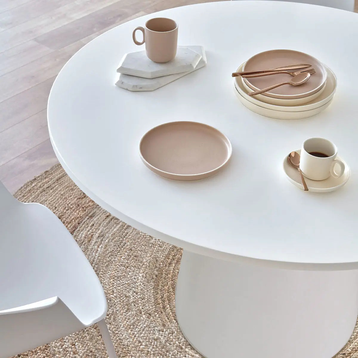 Dwen Modern Round Pedestal Dining Table with white chair, beige rug, and wooden flooring.