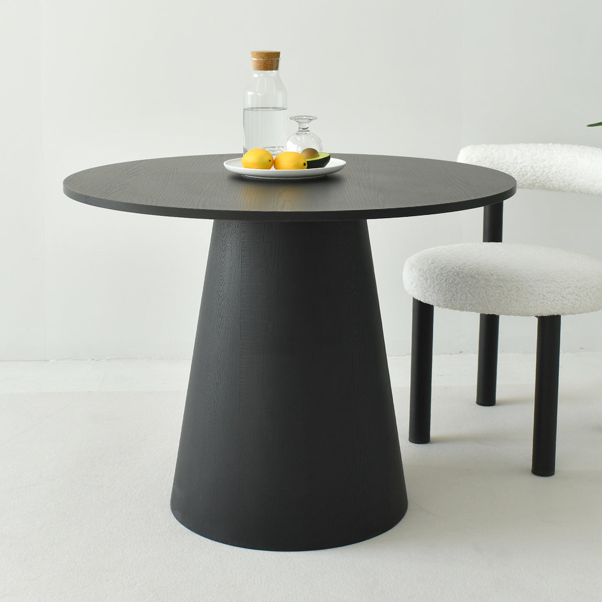 Dwen Modern Round Pedestal Console Table with black finish, white chair, on light carpet flooring.