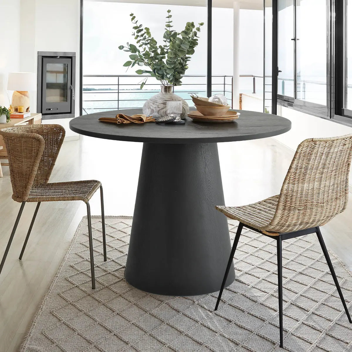 Dwen Modern Round Pedestal Dining Table with wicker chairs, neutral rug, in spacious dining room.