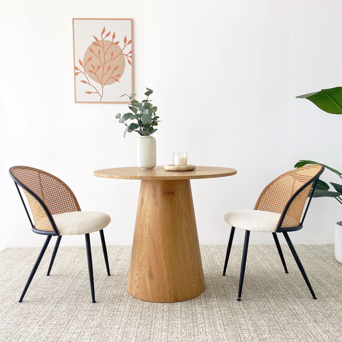 Dwen Modern Round Pedestal Dining Table with natural wood finish, paired with two beige accent chairs.