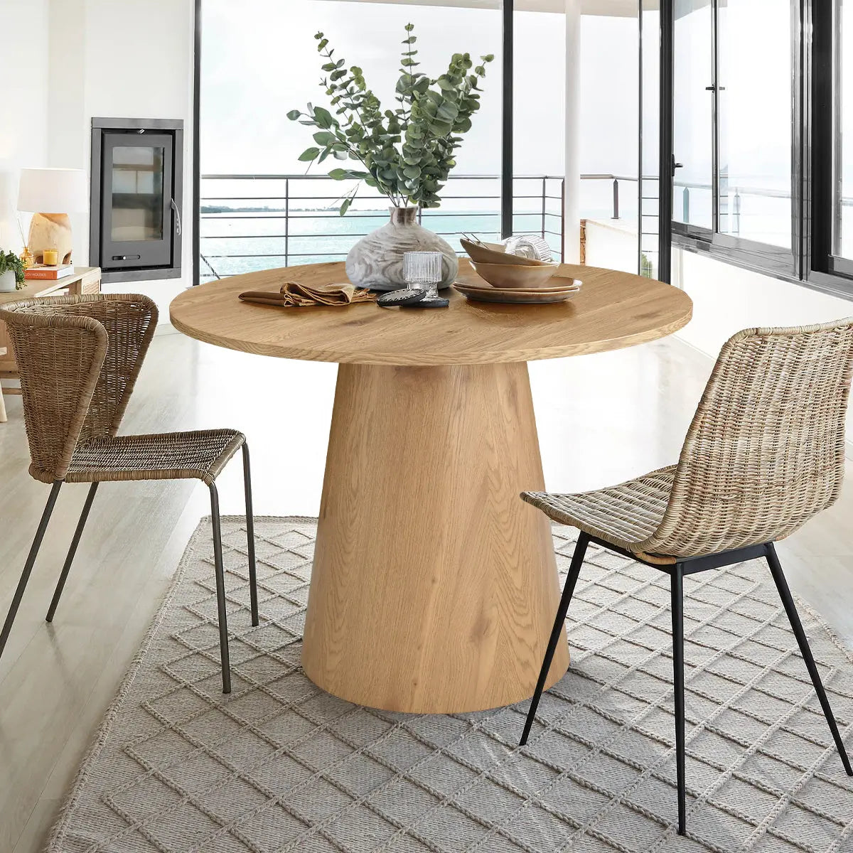 Dwen Modern Round Pedestal Dining Table with wicker chairs, light wood flooring, elegant dining room.