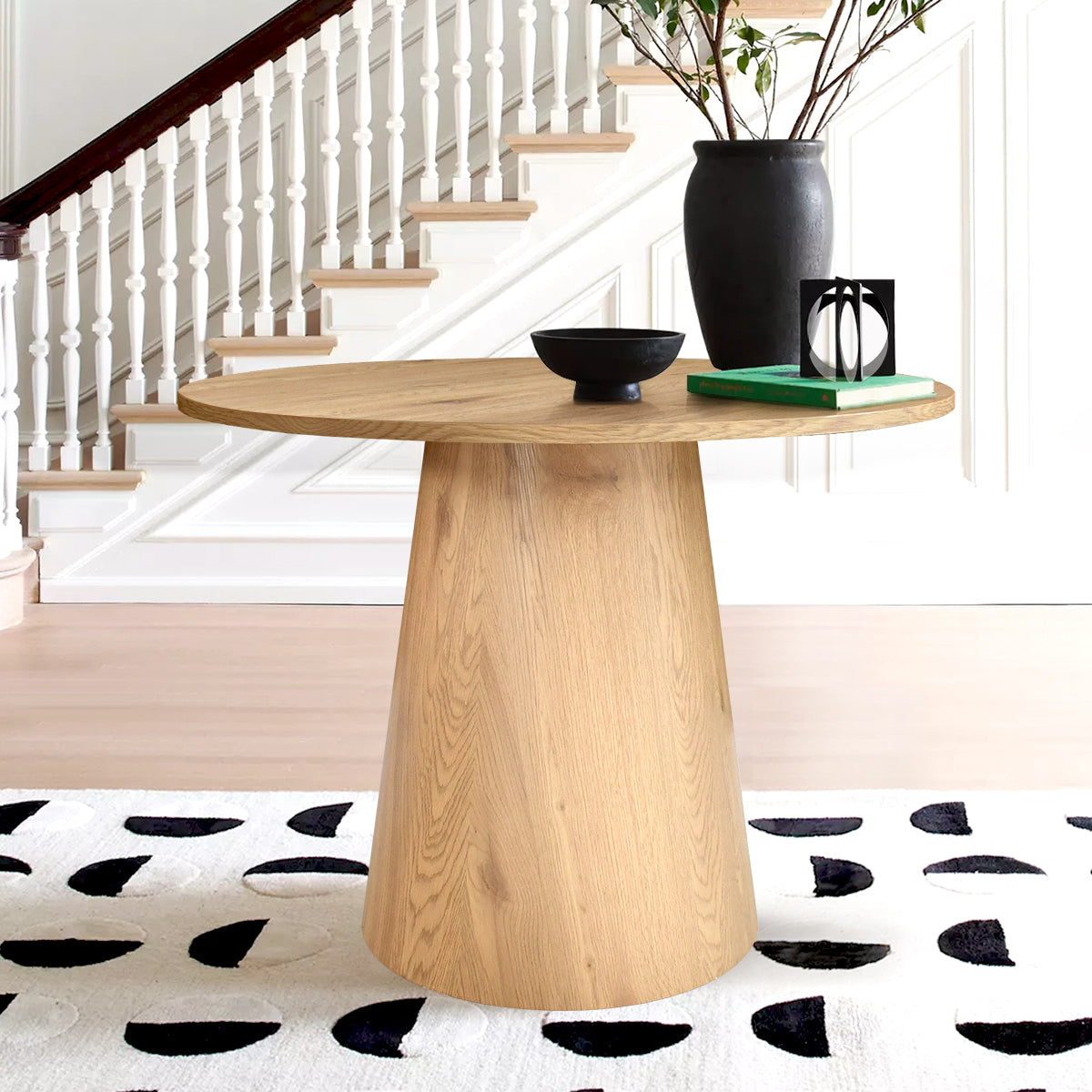 Dwen Modern Round Pedestal Console Table in entryway with patterned rug and staircase backdrop.