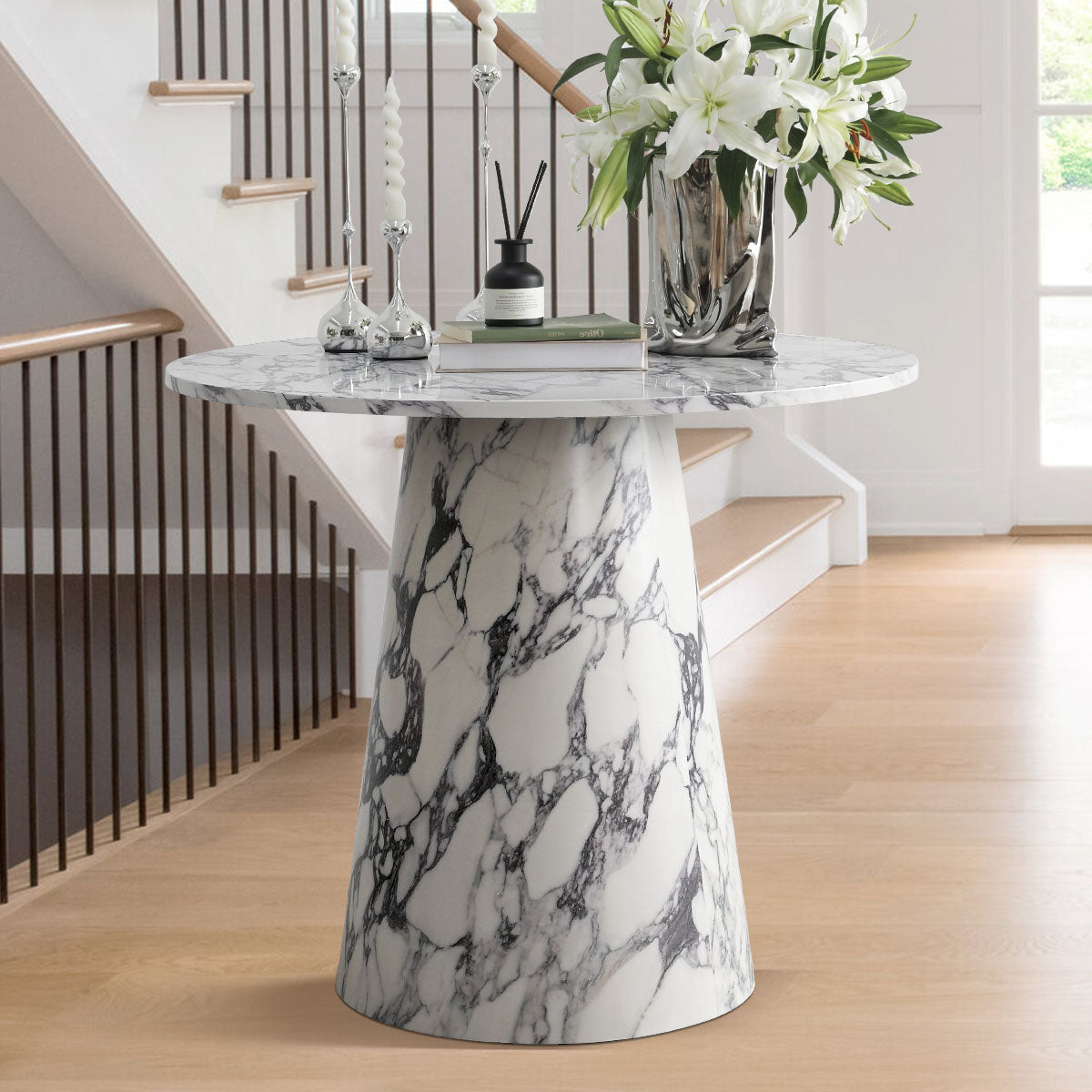 Dwen Modern Marble Round Dining Table with pedestal base, light wood flooring, white walls, stairway backdrop.