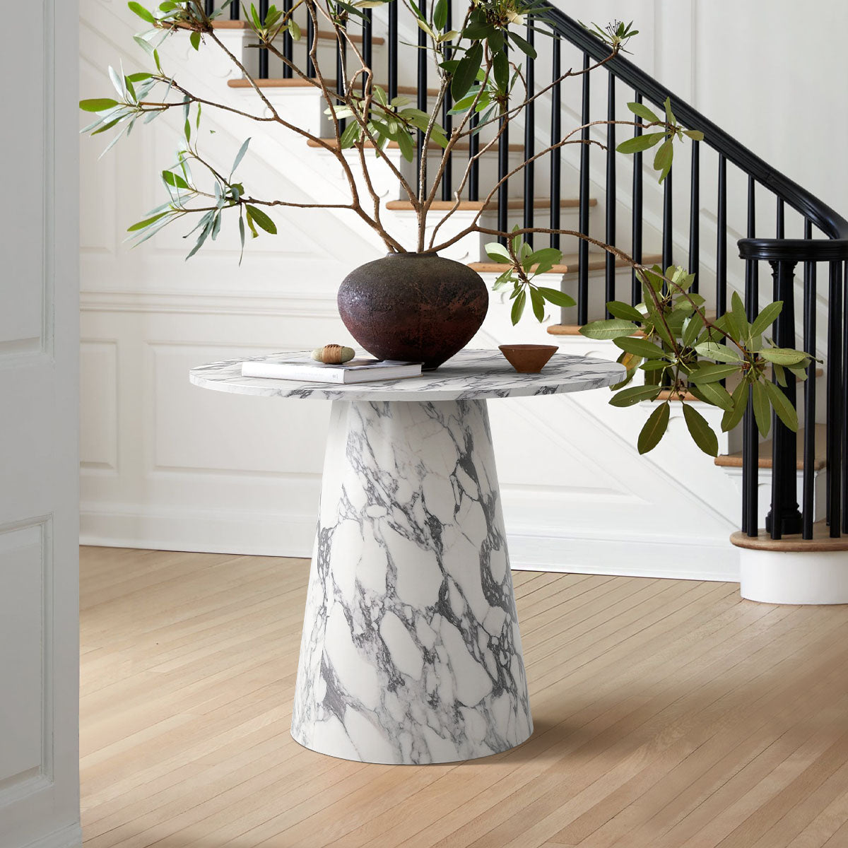 Dwen marble round pedestal dining table, wooden flooring, elegant staircase, contemporary room setting.