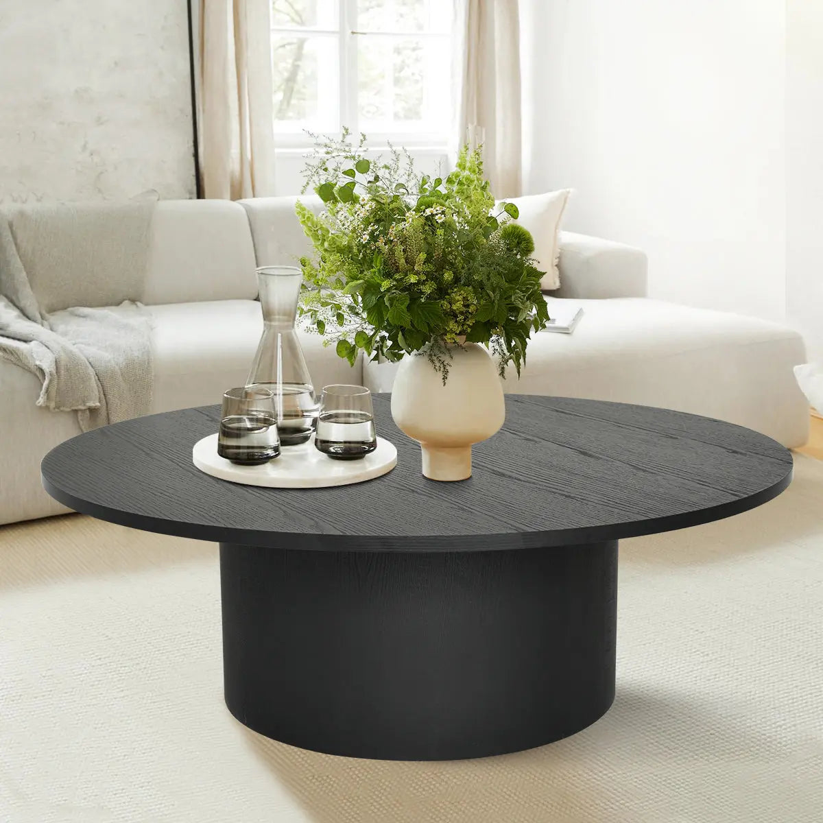 Dwen Modern Round Pedestal Coffee Table in cozy living room with beige sofa and light carpet.