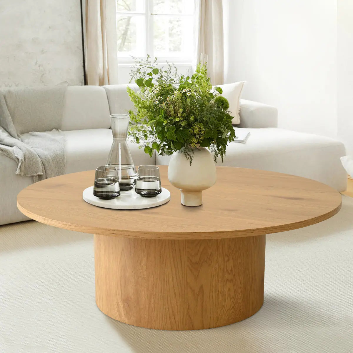 Dwen 40" round pedestal coffee table in modern lounge; light sofa, textured wall, soft carpet.