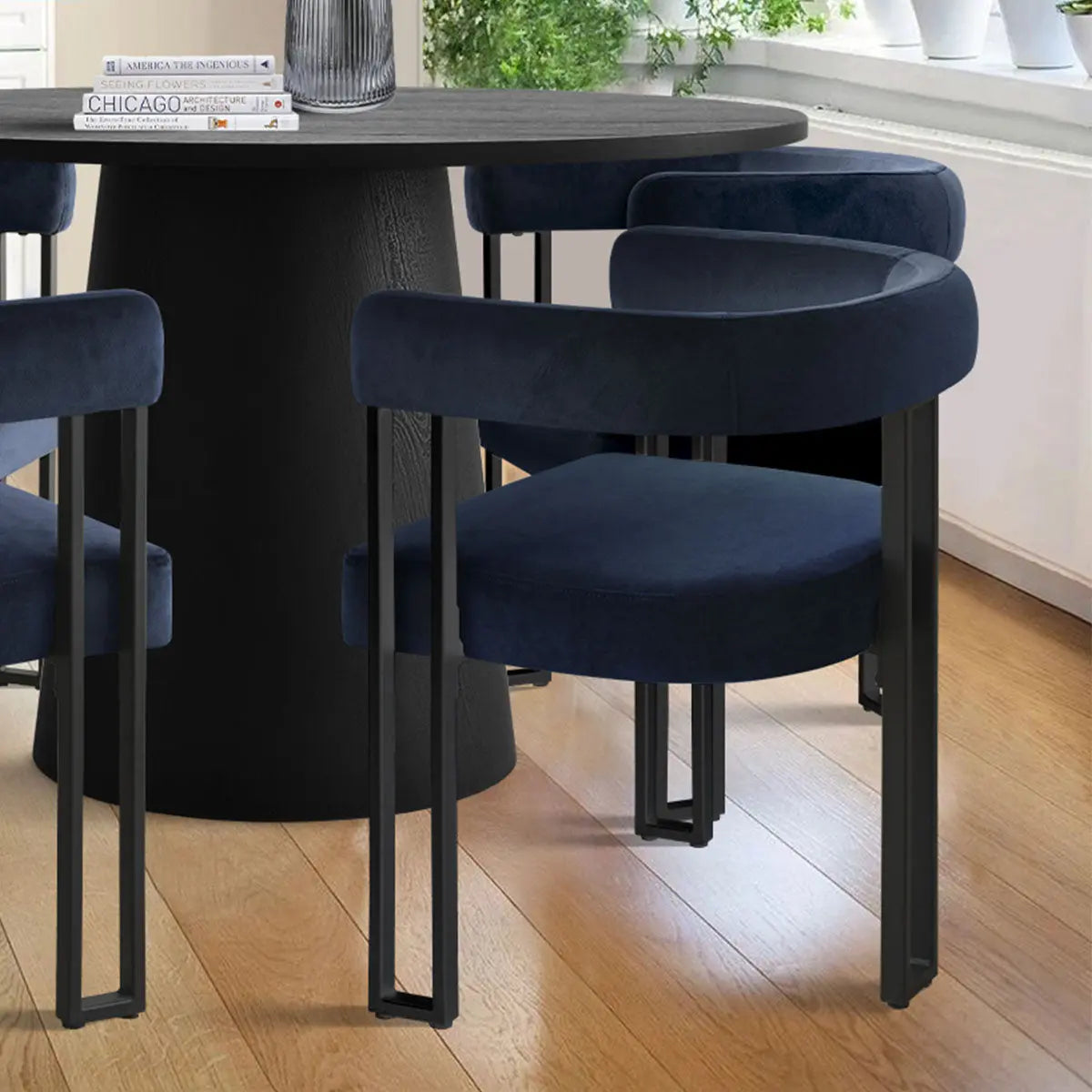 Dwen & Mia Dining Table Set with black velvet chairs, wood flooring, white walls, green decor.