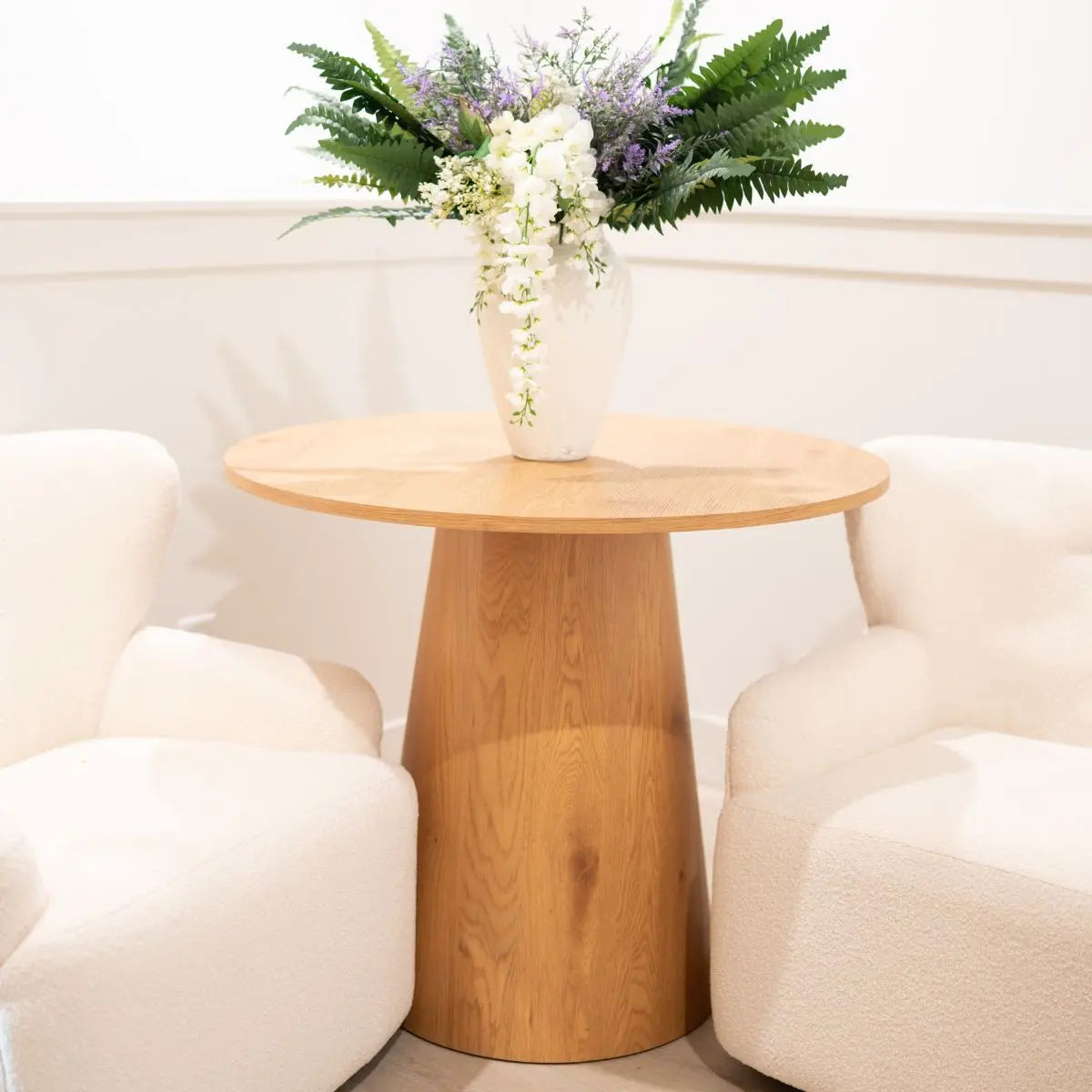 Dwen 35" round pedestal dining table, white armchairs, wood floor, white walls, floral decor.