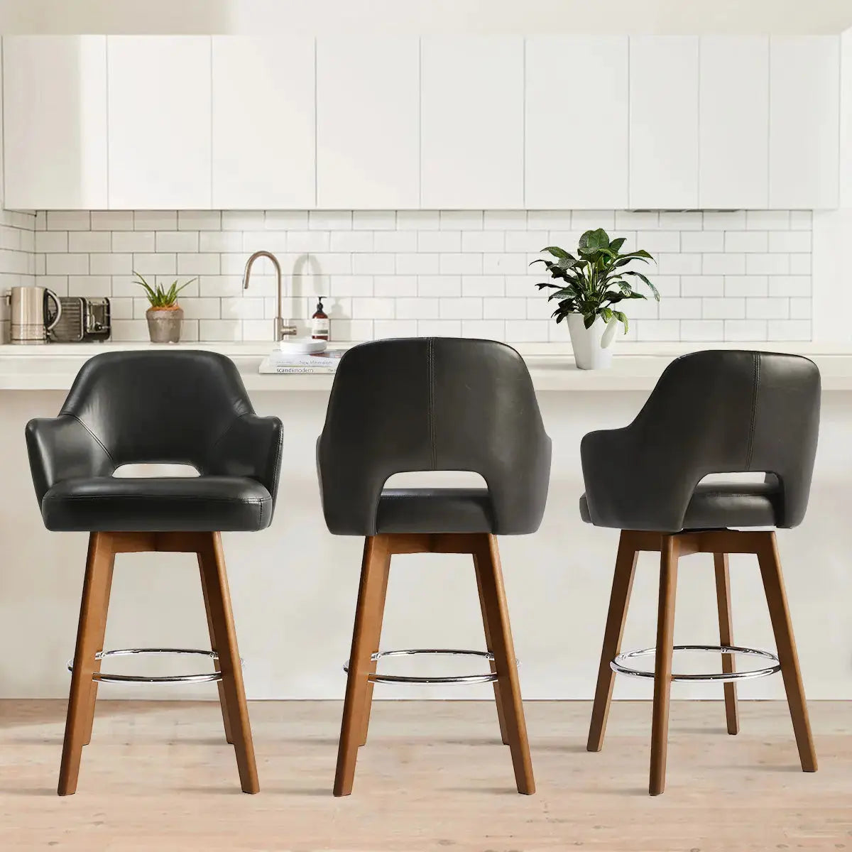 Three Edward Leather Swivel Counter Stools with Arms in kitchen with white cabinets and wood flooring.