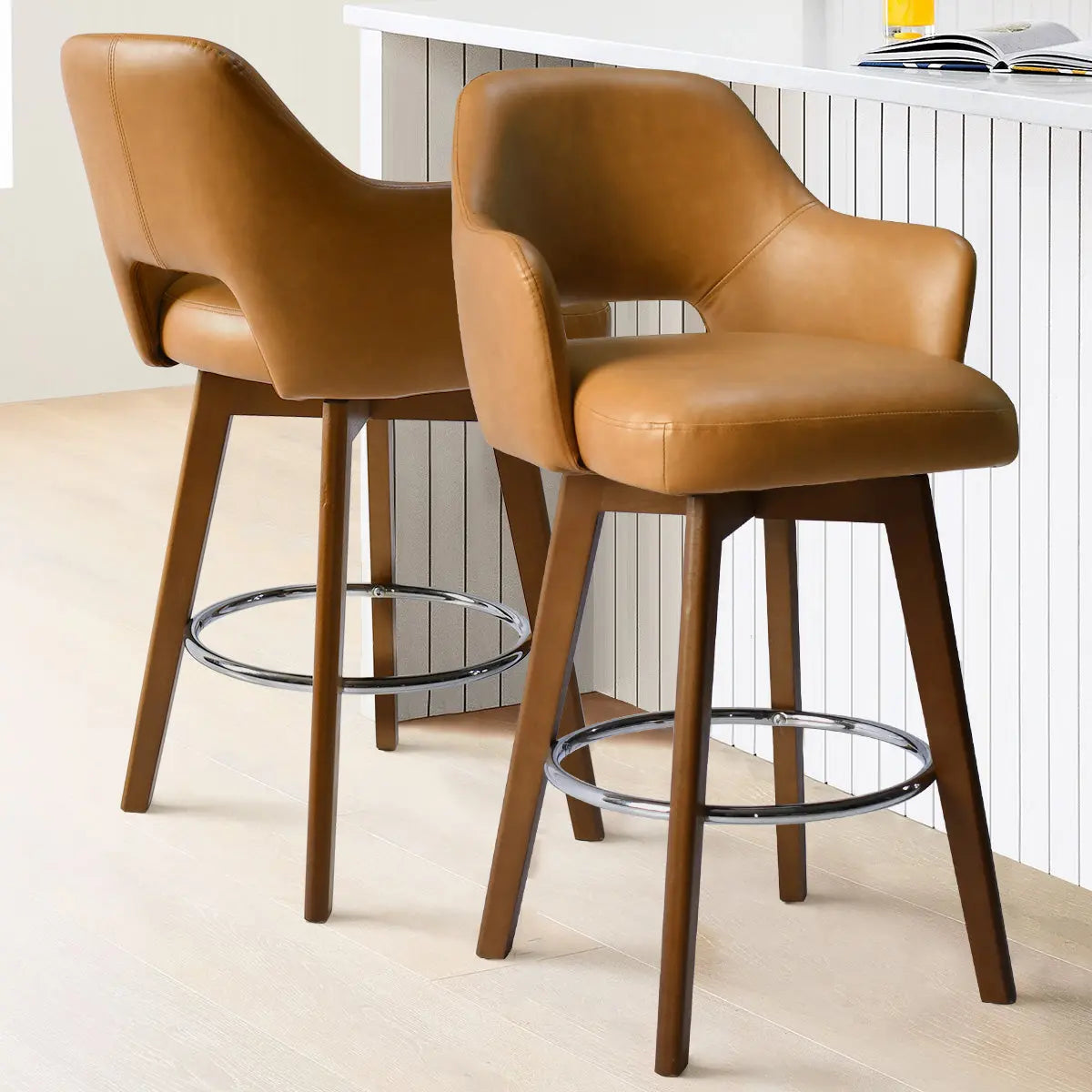 Two Edward Leather Swivel Counter Stools with Arms in kitchen, light wood flooring, paneled island.