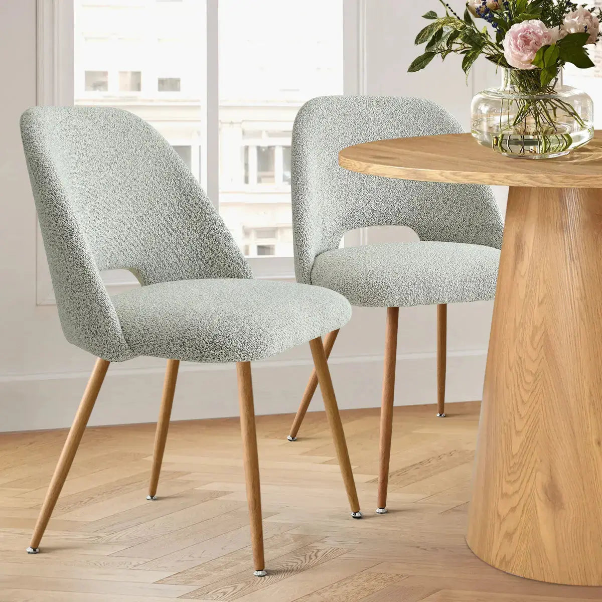 Edwin dining chair, modern upholstery, light wood legs, next to round wooden table, parquet flooring.