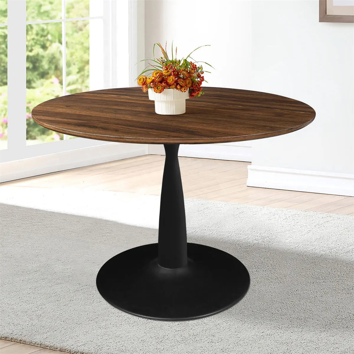 Harold Modern Round Pedestal Dining Table in bright room, light wood flooring, white walls, beige carpet.