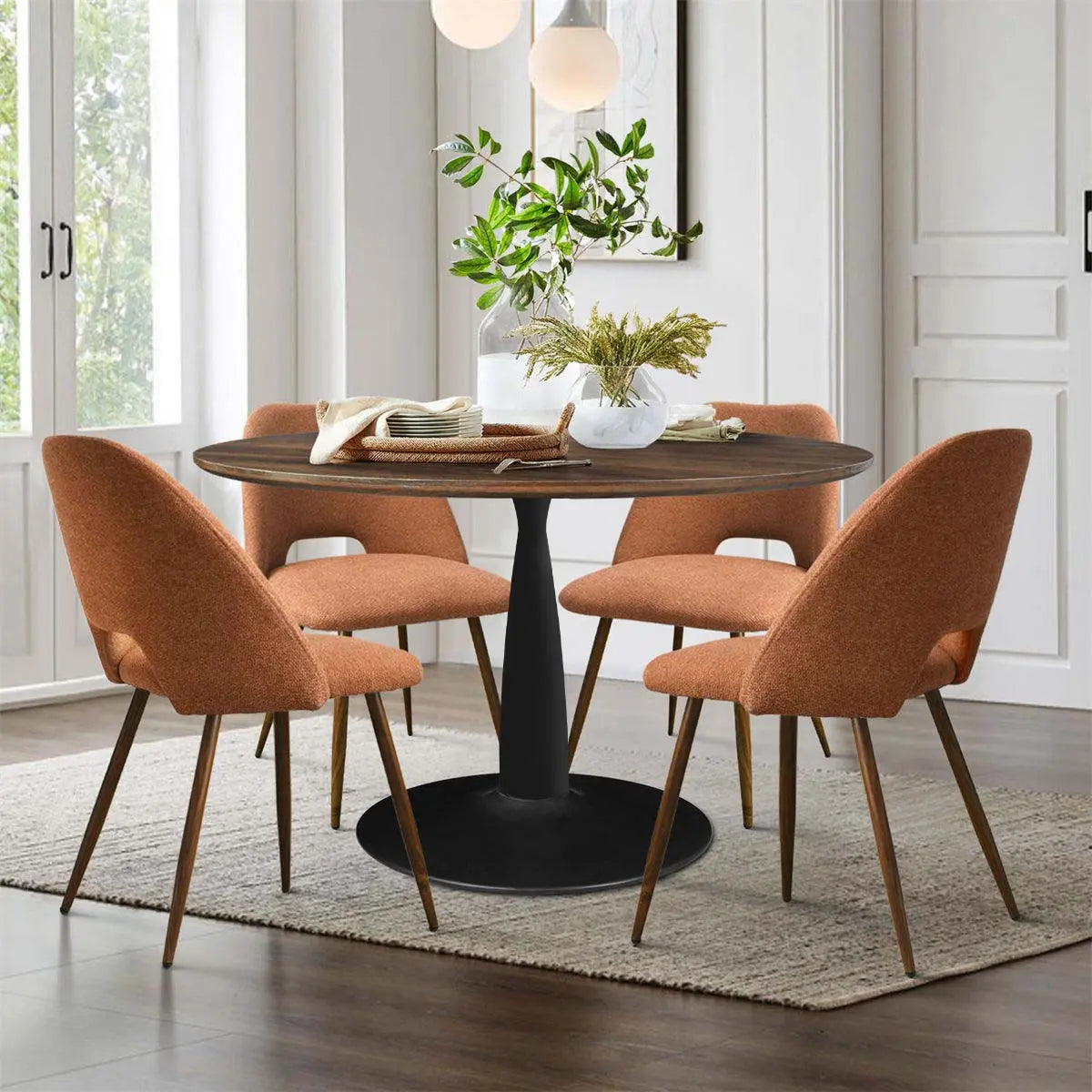 Harold & Edwin round dining table set with orange chairs, white walls, wood floor, dining room.