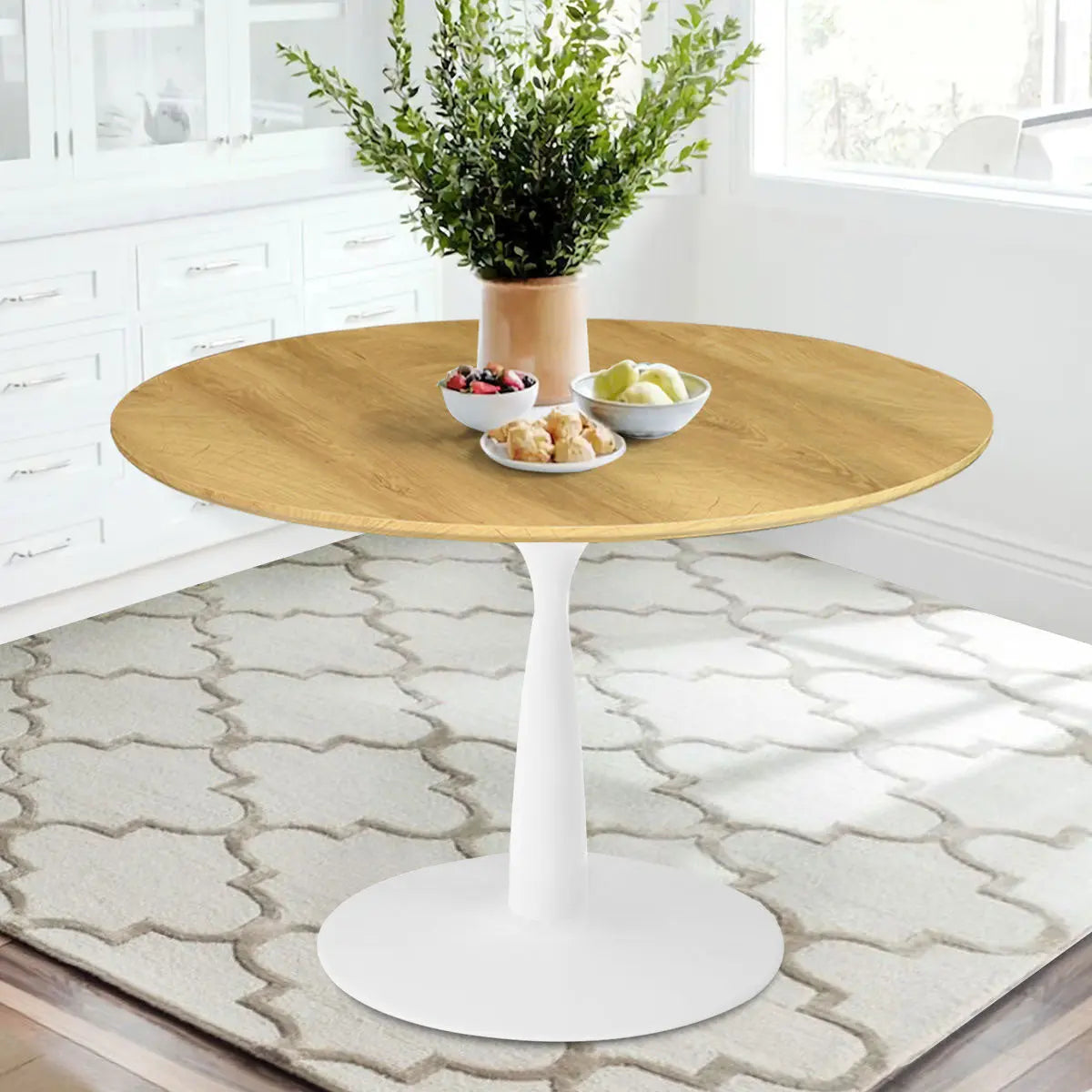 Harrison Modern Oak Round Dining Table in bright room, beige patterned rug, white cabinetry, natural light.