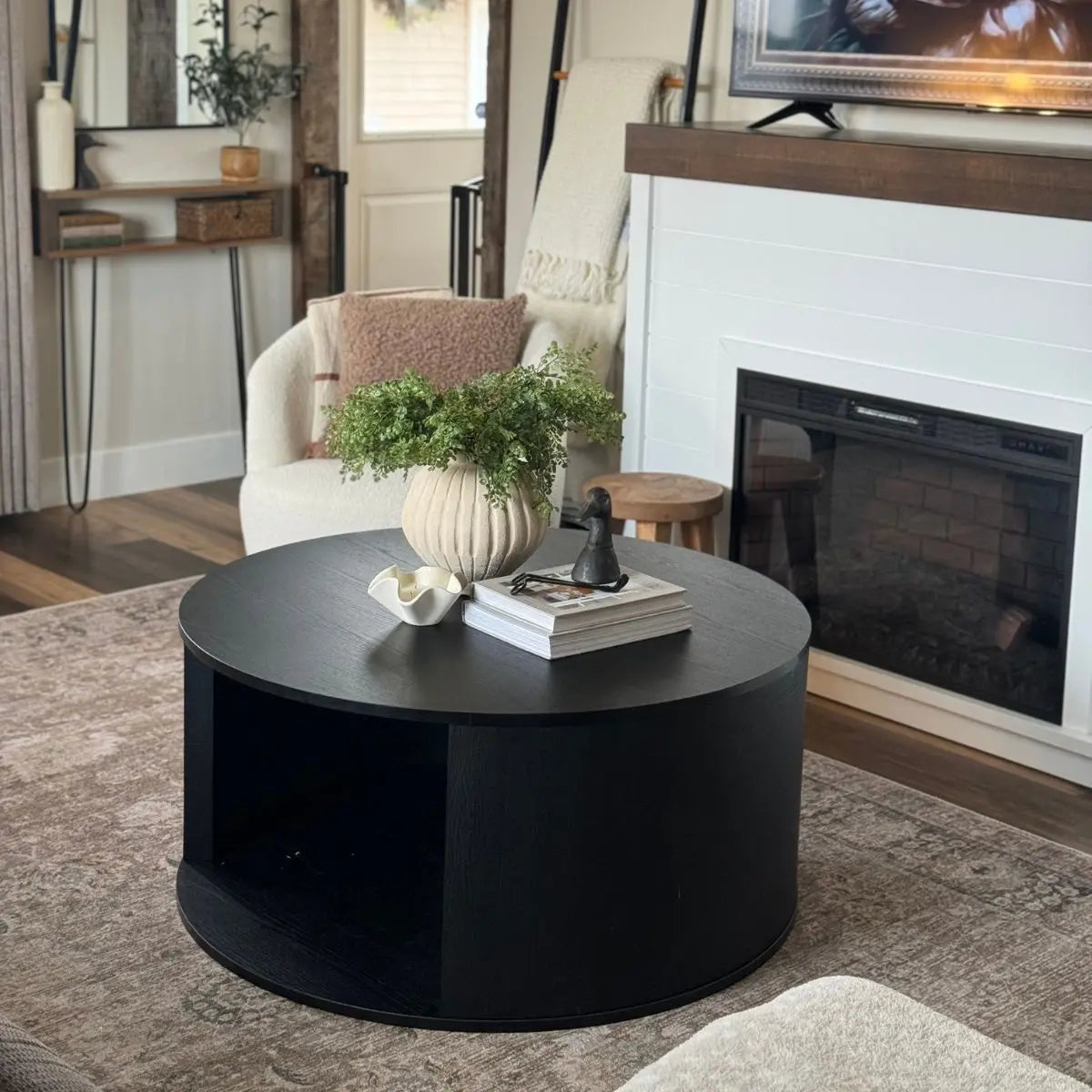 Modern black round coffee table in cozy living room with fireplace, white walls, and beige sofa.