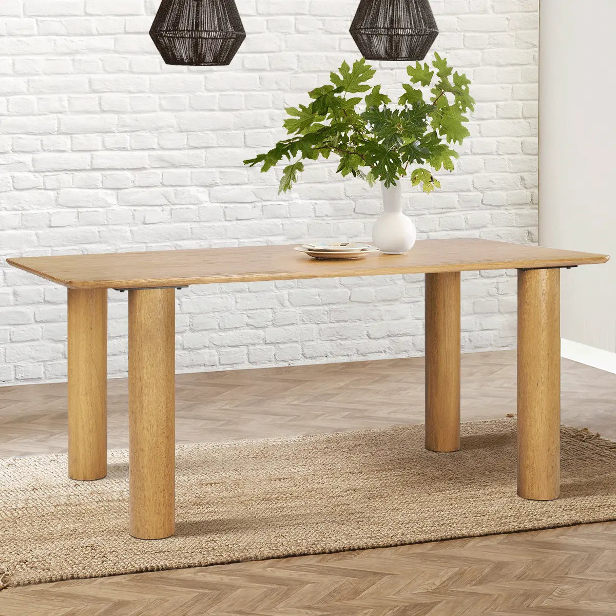 Johson 67" oak dining table on patterned rug, white brick wall, wicker pendant lights.