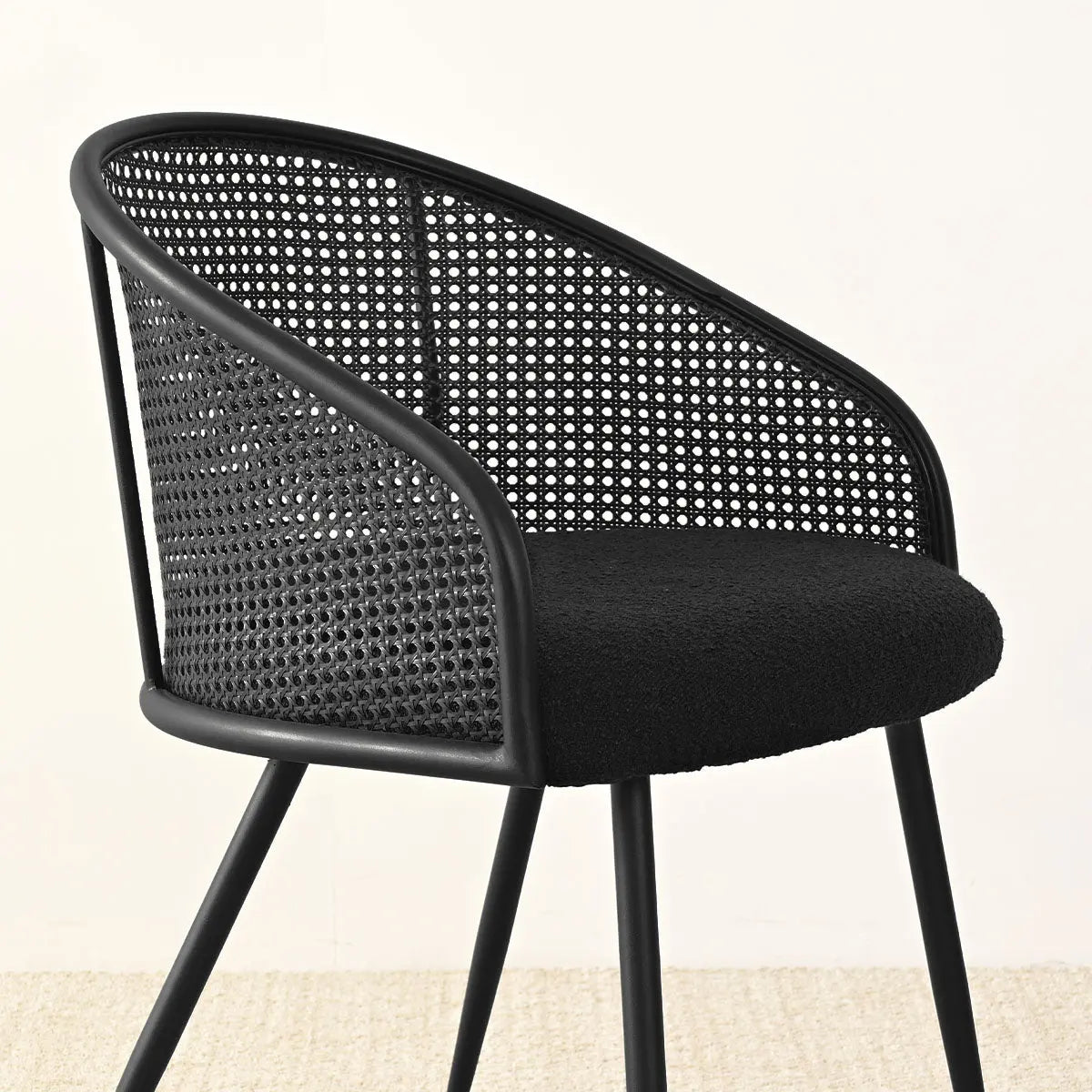 Jules Modern Upholstered Rattan Dining Chair with Arms, black, on beige carpet in dining area.