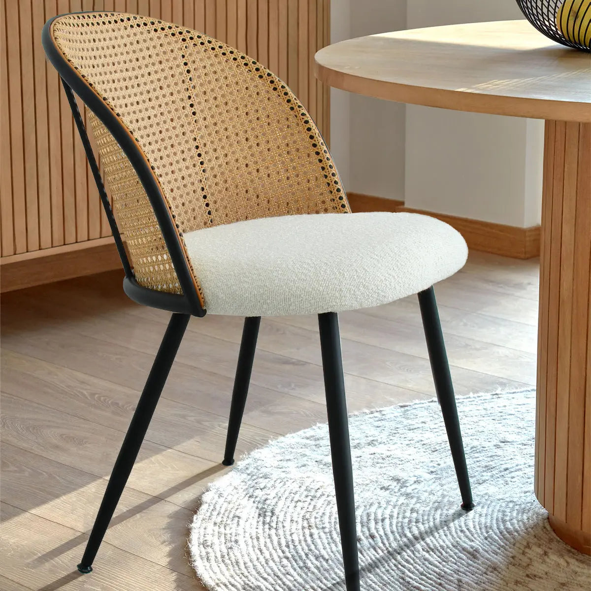 Modern Jules Upholstered Rattan Dining Chair near round table; wooden flooring, light walls, rug visible.