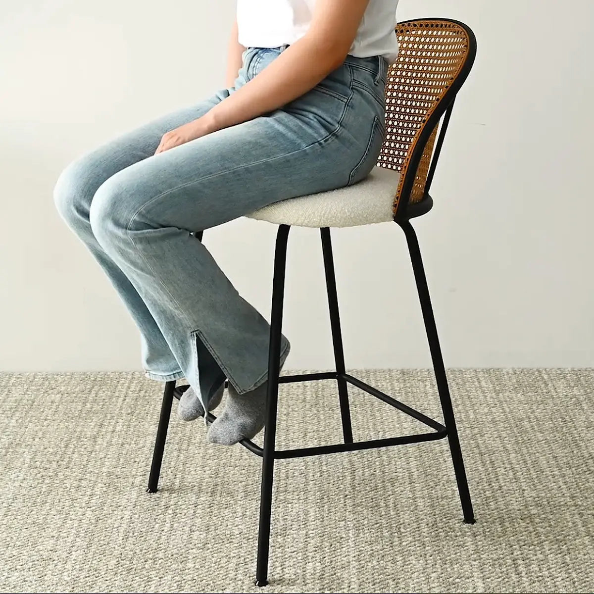 Jules Modern Upholstered Rattan Counter Stool on beige carpeted floor with person seated.