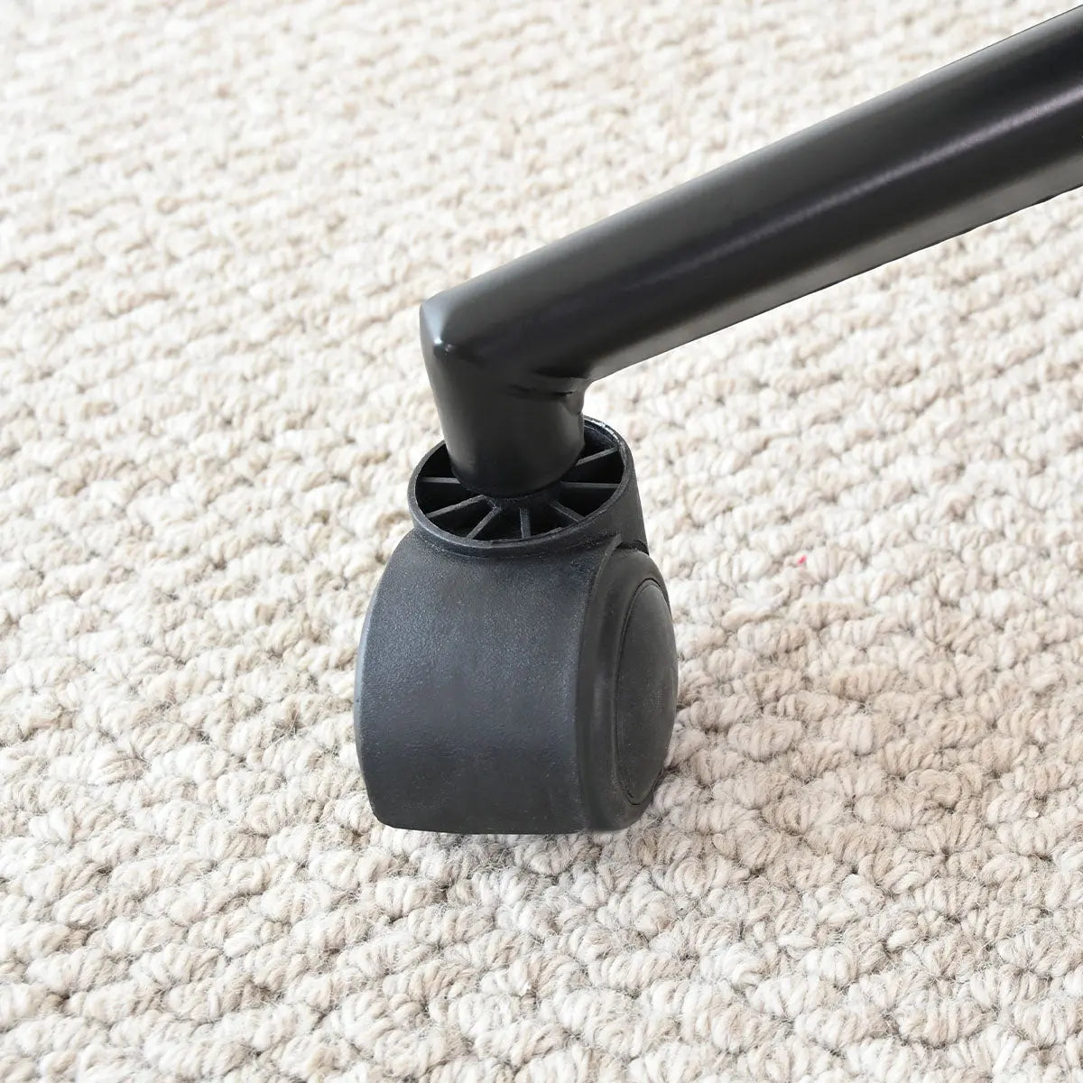 Close-up of the Jules Modern adjustable office chair wheel on textured beige carpet flooring.