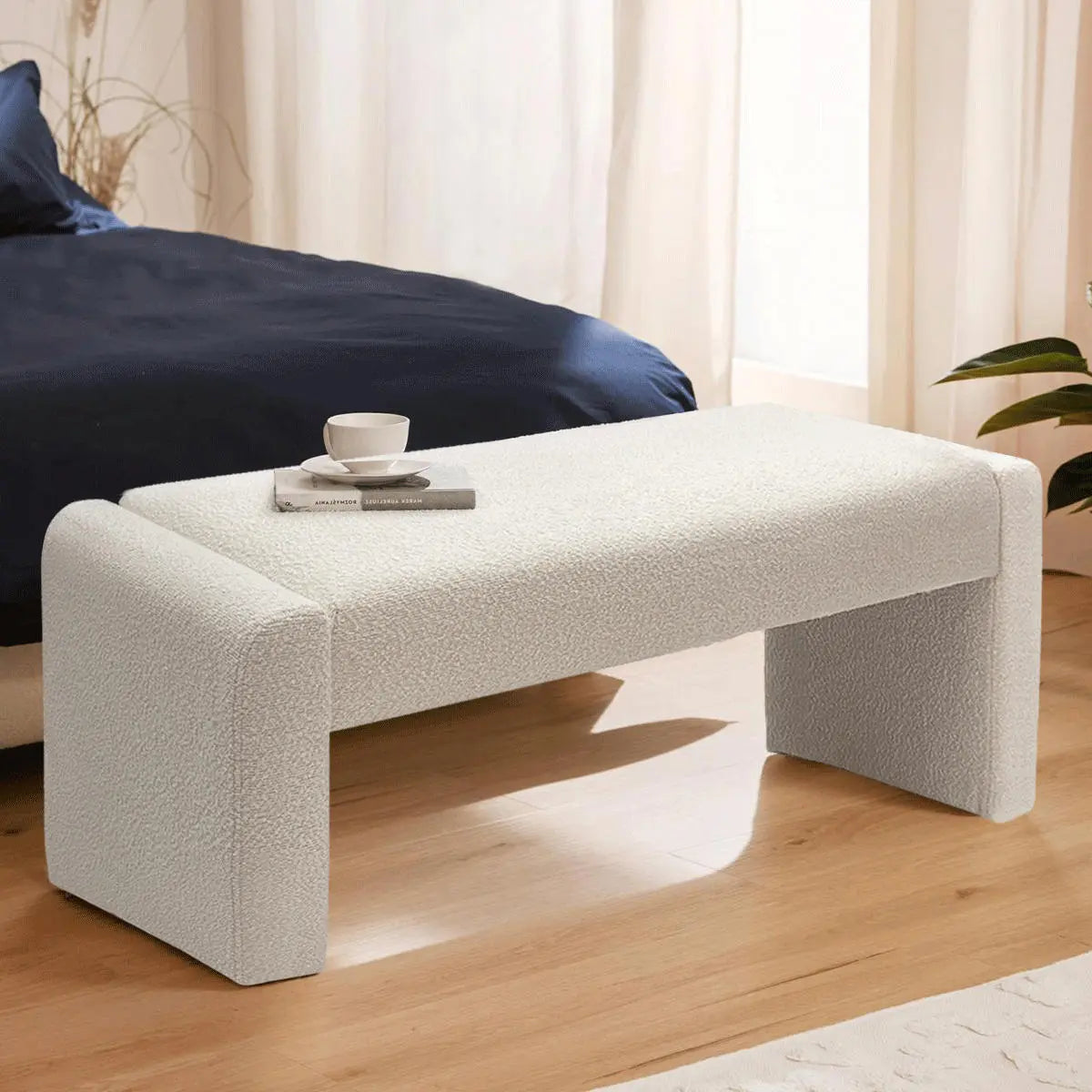 Kaia Modern Beige Upholstered Waterfall Bench, bedroom setting, navy bedding, wooden floor, beige curtains.