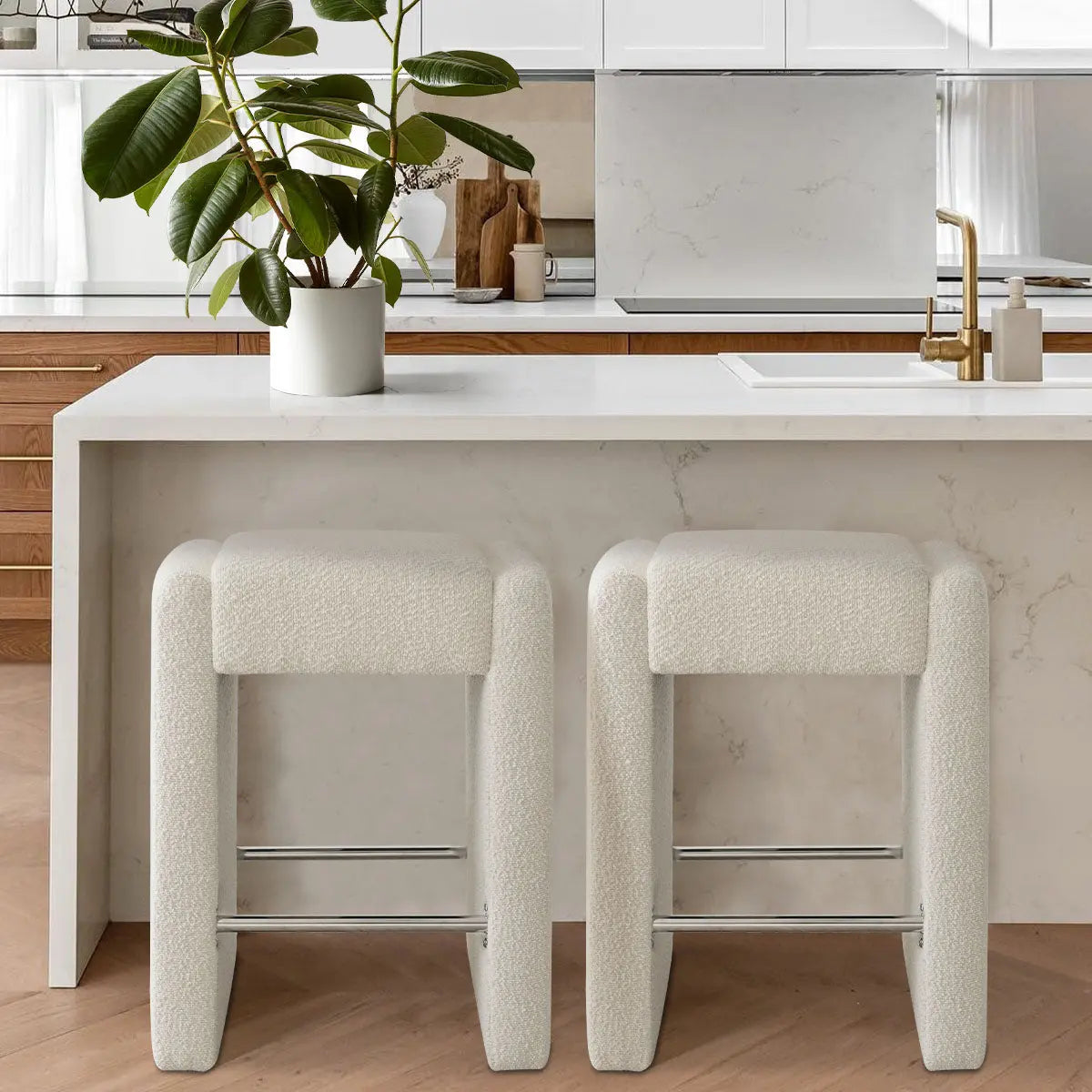 Kaia beige boucle counter stool set in modern kitchen with wood cabinets, marble island, and gold faucet.