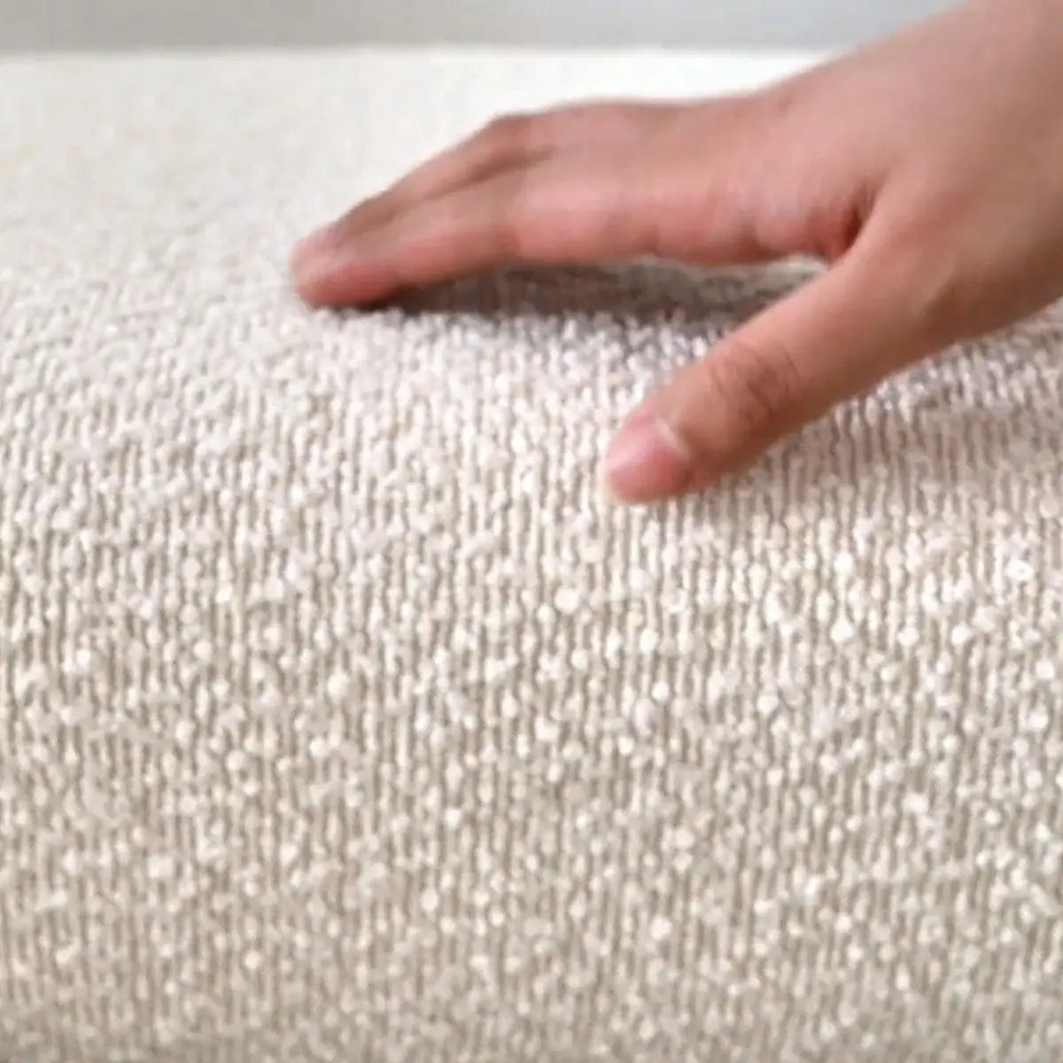 Close-up texture of Kaia Beige Boucle Counter Stool upholstery with hand touching cushion fabric.