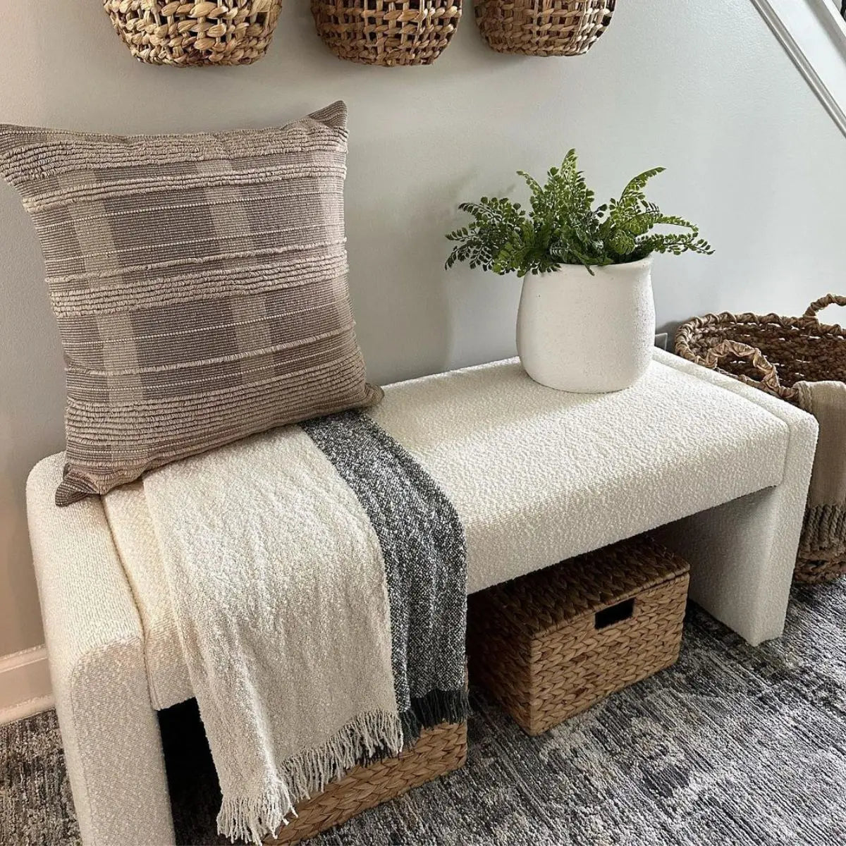 Kaia beige upholstered bench with woven baskets, textured pillow, and gray carpet in neutral room.